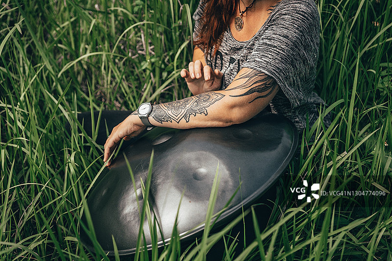 长发女人坐在高高的草丛中演奏手碟图片素材