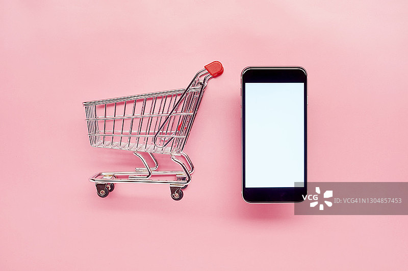 粉色背景上的小型空购物车和手机，在线购物图片素材