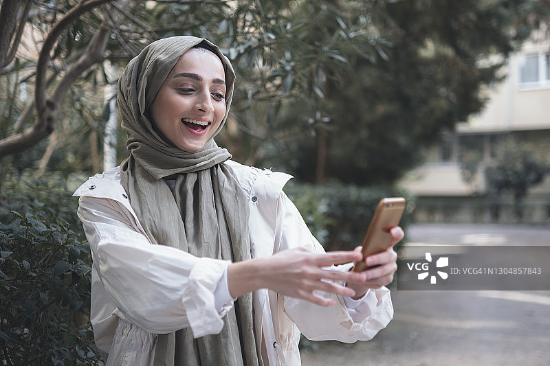 使用智能手机的微笑穆斯林年轻女人 портрет图片素材