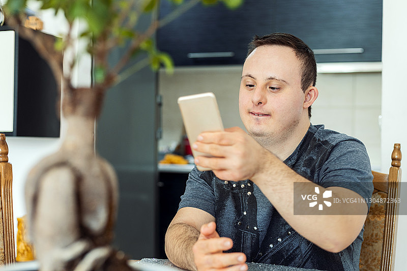 患有唐氏综合征的年轻男子正在使用智能手机图片素材