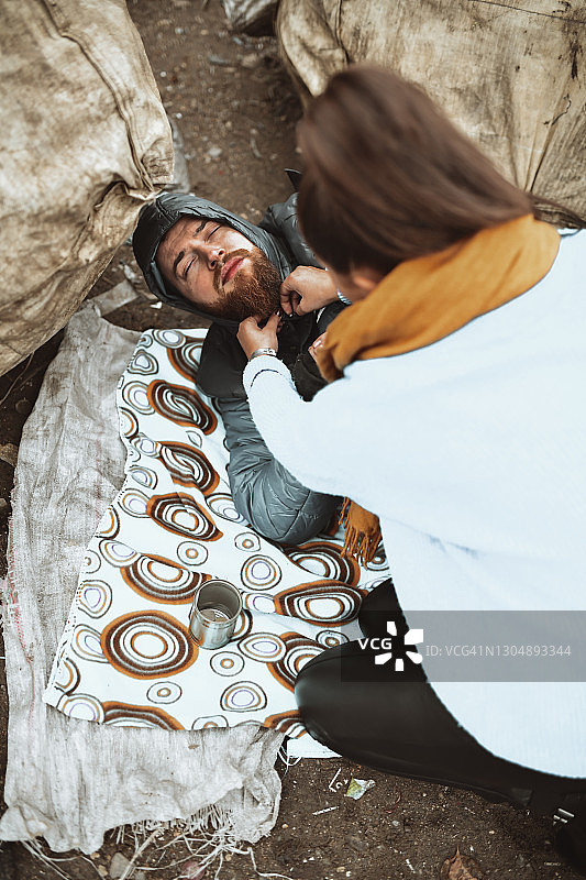 女人照顾无家可归的男人并拉上夹克图片素材
