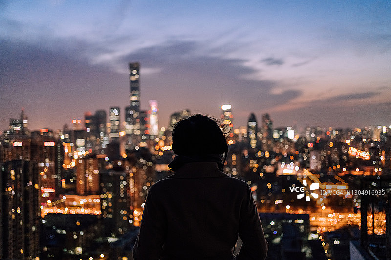 夜晚，女人站立在现代城市前图片素材