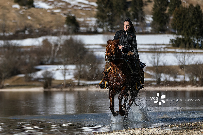 傍晚，女孩在河岸边的水中骑马图片素材
