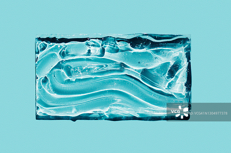 蓝色背景玻璃上保湿化妆凝胶的抽象涂抹特写。扁平风格。化妆品banner。年度潮流程序概念图片素材