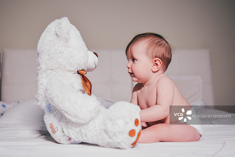 坐在床上玩泰迪熊的女婴图片素材