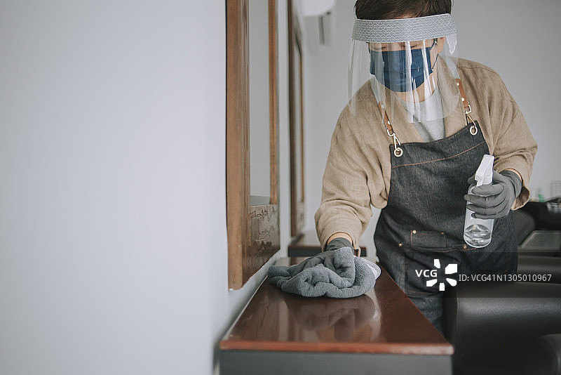 中国理发店老板戴着防护面罩和手套清洁消毒，为重新开业做准备图片素材