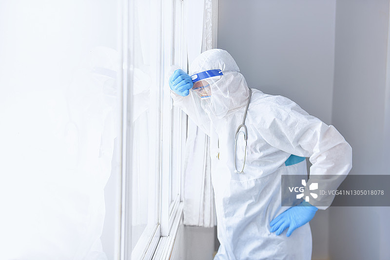 疲惫的医生在泰国靠窗户休息，戴着个人防护装备图片素材