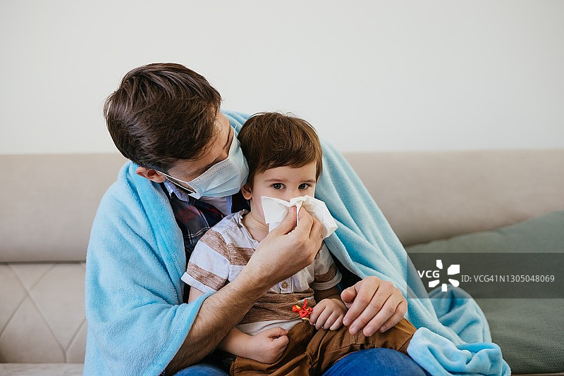 父亲拿着纸巾，可爱的男孩在室内擤鼻涕图片素材