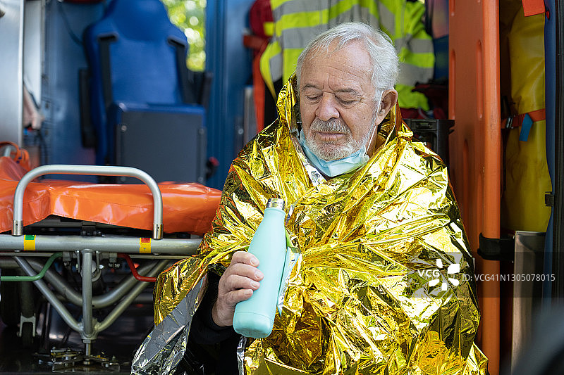 年长的男人坐在盖着急救毯的救护车上图片素材