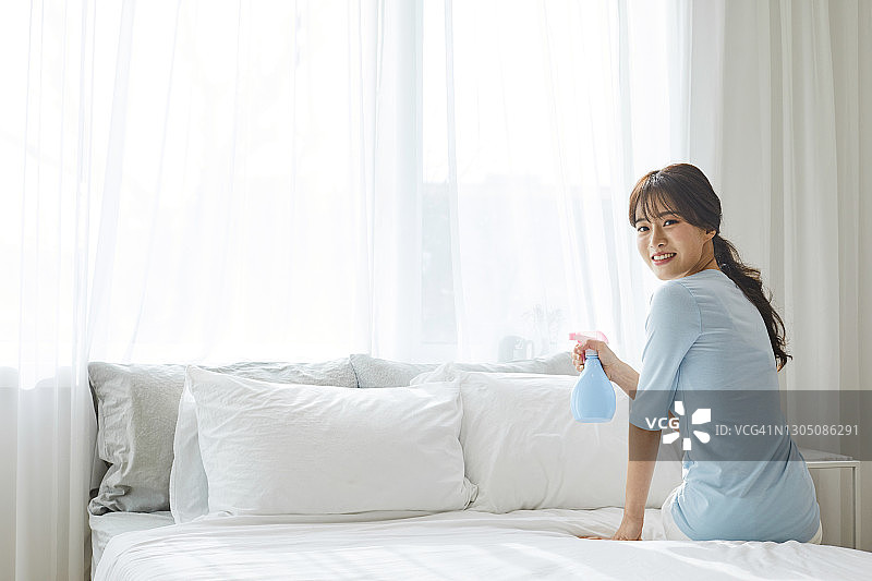 女人在床上用品上喷洒清新剂图片素材