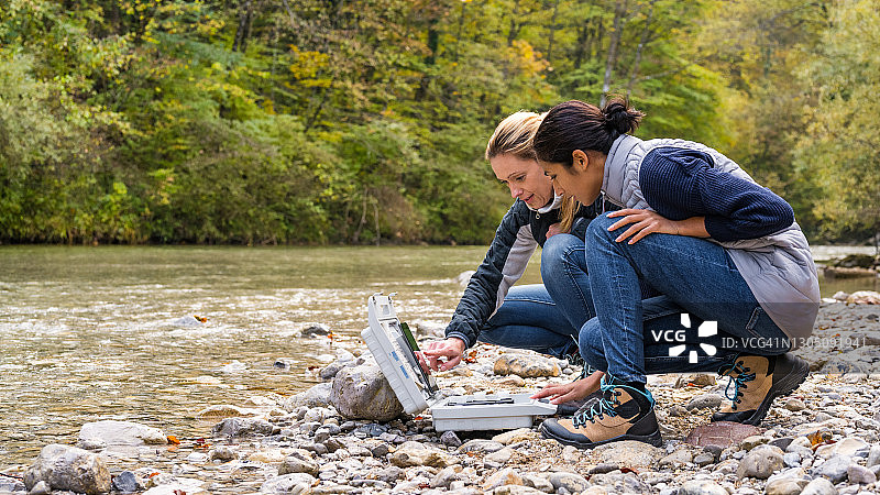 女同事们在数字平板电脑中讨论数据，两位女士蹲在河边图片素材