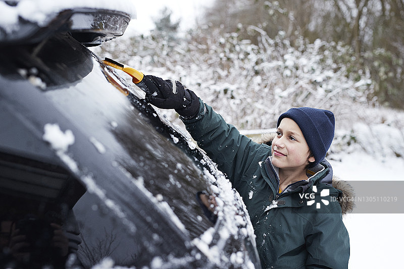 男孩用刮刀清除汽车挡风玻璃上的积雪图片素材