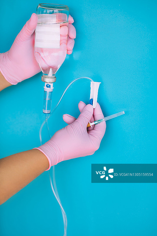 蓝色背景下，戴着粉色手套的医生手中的盐水滴管系统。新冠病毒隔离和医疗概念图片素材