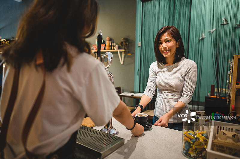 年轻的亚洲咖啡师在柜台为顾客提供咖啡图片素材