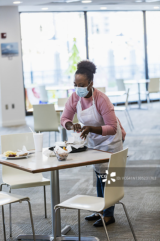 在自助餐厅戴着口罩清洁桌子的女服务员图片素材