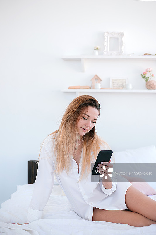 在卧室床上用手机的年轻女子图片素材
