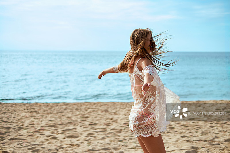 穿连衣裙的年轻女人在沙滩上张开双臂跳舞图片素材