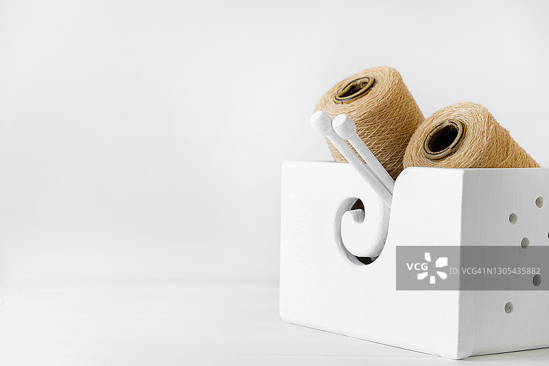 米色意大利羊毛纱线、线团和线轴，白色背景木箱中的针织针。针织、手工、爱好概念。文本空间副本。图片素材