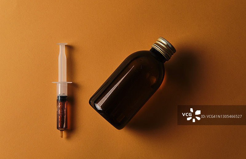 黄色背景下的止咳糖浆瓶及其饮用注射器图片素材