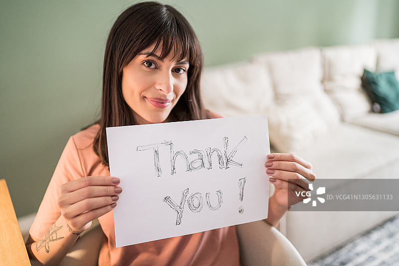 年轻女子在家手持写着“谢谢”的纸的肖像图片素材