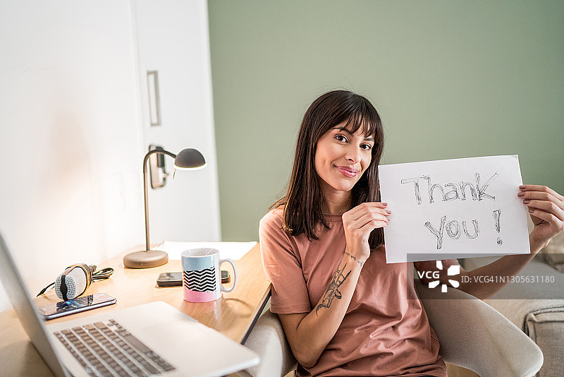 年轻女子在家手持写着“谢谢”的纸的肖像图片素材