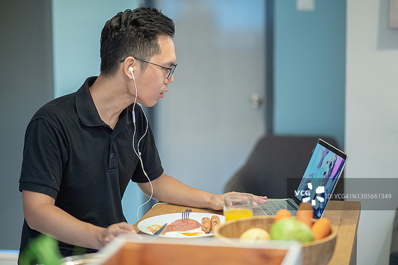 在餐厅使用笔记本电脑在家工作的亚洲成年男人图片素材