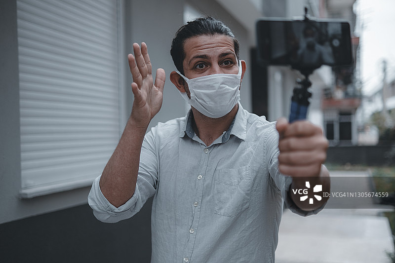 年轻男人戴着医用口罩用智能手机拍摄vlog图片素材