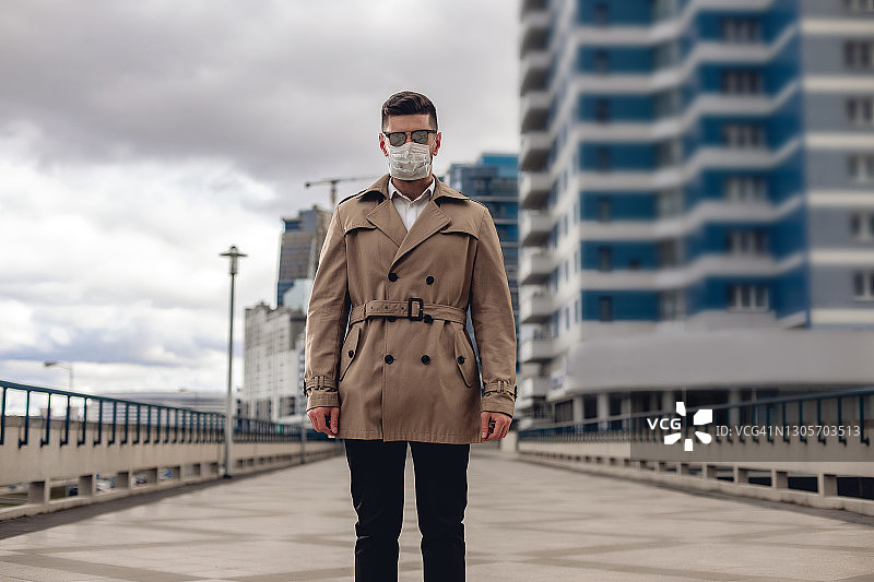街上穿着米色夹克和白衬衫的络腮胡白人男子肖像。戴防护口罩和黑色时尚太阳镜的男士图片素材