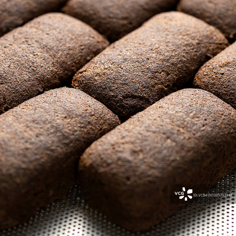 成排的完整黑面包。面包背景。特写。新鲜烘焙的全麦面包。中心选择性聚焦。食品概念。正方形格式或1x1，用于在社交媒体上发布图片素材