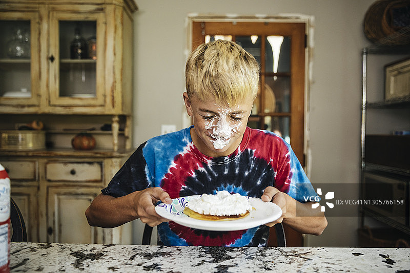 男孩脸上沾着搅打奶油，拿着一盘薄煎饼图片素材