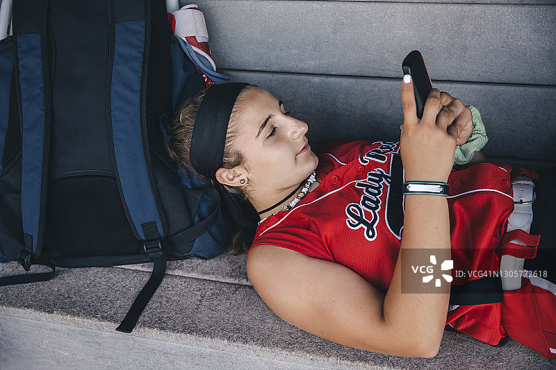 在棒球休息区长椅上用手机的少女图片素材