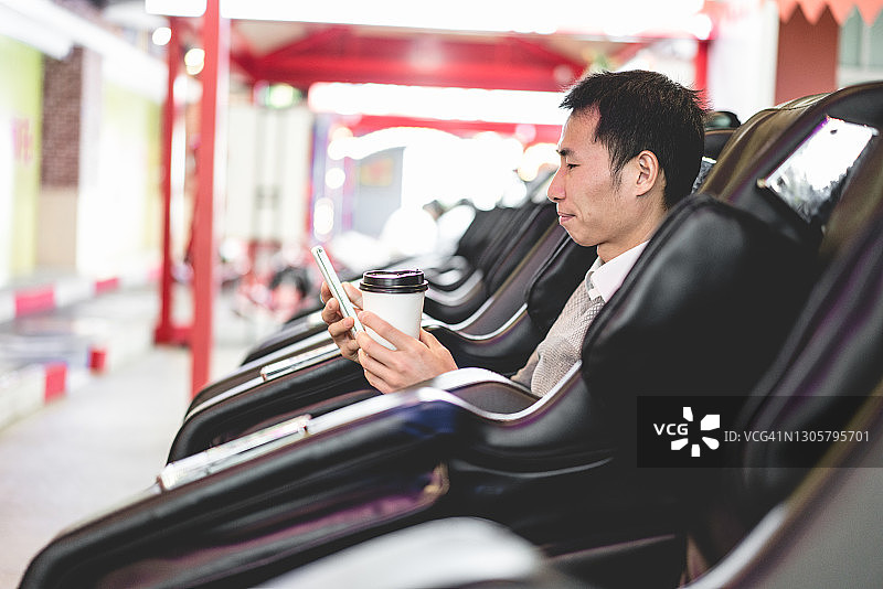 亚裔男人在自动按摩椅上使用智能手机图片素材