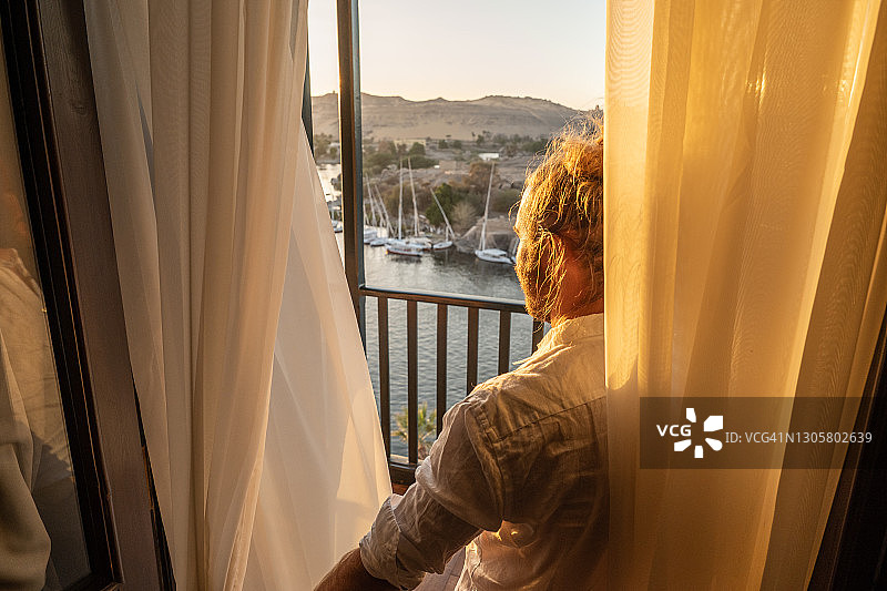日出时，男子在酒店房间里拉开窗帘，尼罗河图片素材
