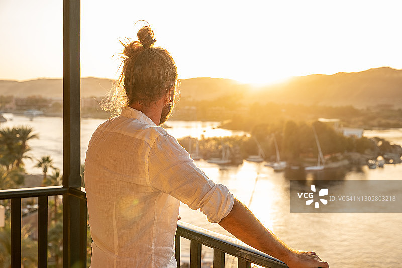 日出时，男子在酒店房间里拉开窗帘，尼罗河图片素材
