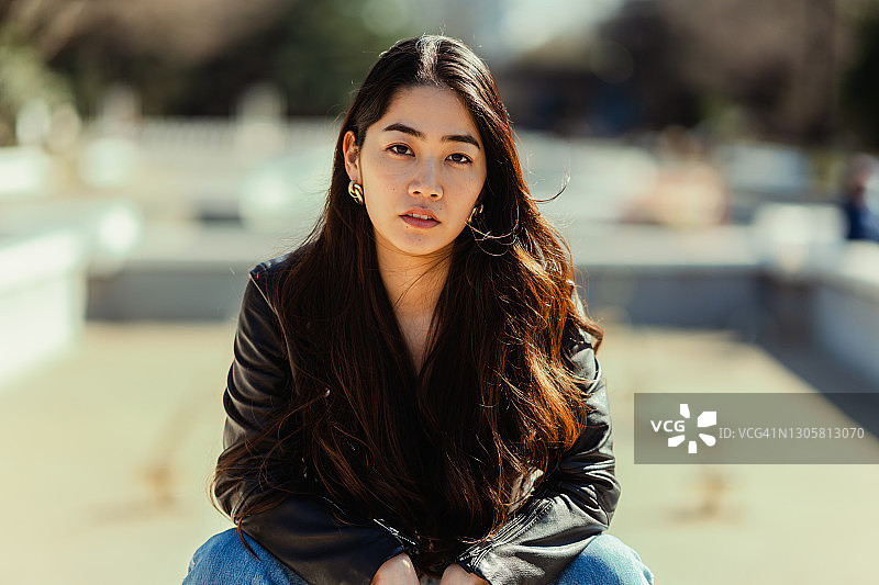 坐在公园里看着镜头的年轻漂亮酷女郎肖像图片素材