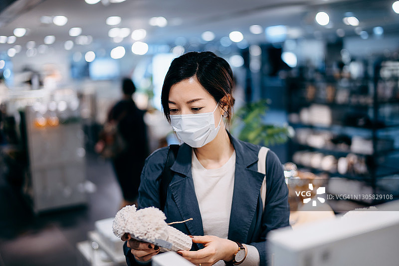 戴防护口罩的亚洲年轻女人在商店购买家居用品，挑选有机毛巾图片素材