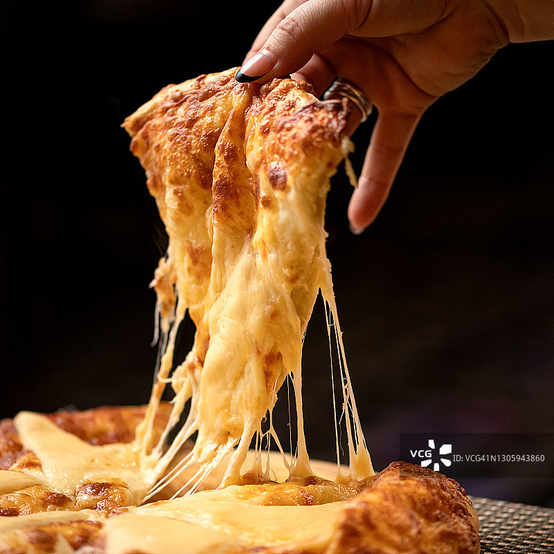 热披萨上的融化奶酪拉丝，女人拿一片披萨。美味的披萨，传统意大利美食，特写镜头。营养晚餐或午餐图片素材