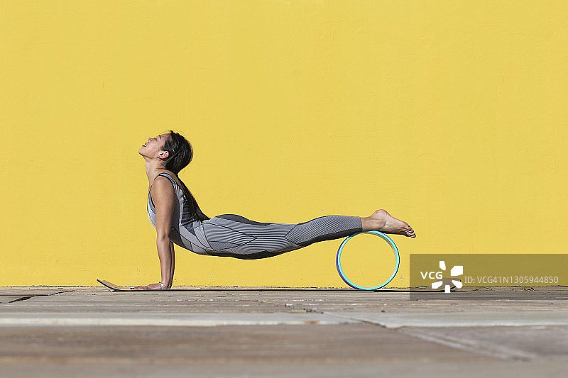 靠在黄色墙壁旁，用瑜伽轮锻炼的女人图片素材
