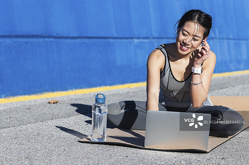 坐在运动垫上使用笔记本电脑的微笑女人图片素材