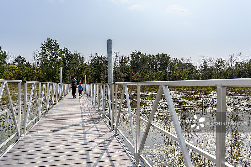 母亲和儿子在加拿大魁北克省普莱桑斯国家公园跨过水上的木桥图片素材