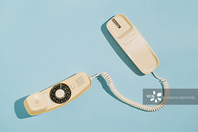 蓝色背景上，摘机的黄色拨盘电话的俯视图图片素材