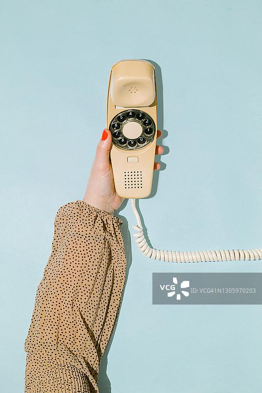 蓝色背景上手持老式黄色拨盘电话听筒的女人手部特写图片素材