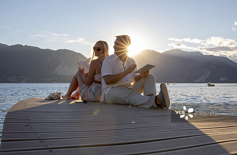 一对夫妇一起阅读在码头上的湖，日出图片素材
