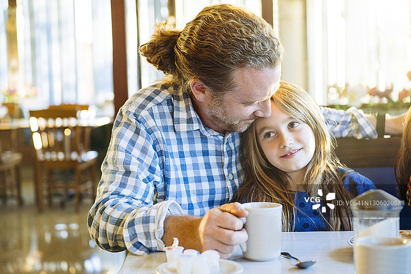 父亲在餐馆的桌旁拥抱女儿图片素材