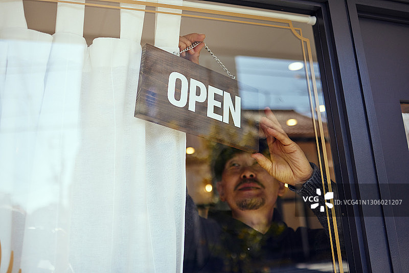 男性店主在玻璃门上悬挂“开放”标志图片素材