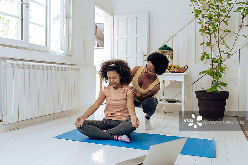 快乐的非洲裔女孩在母亲的帮助下练习瑜伽图片素材