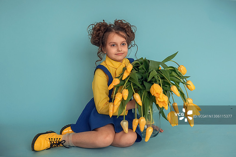 蓝色背景下手捧黄色郁金香花束的女孩图片素材