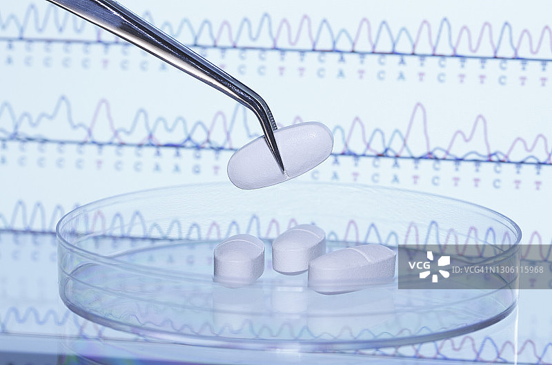 镊子夹着药丸，背景是显示DNA自动测序结果的电脑屏幕图片素材