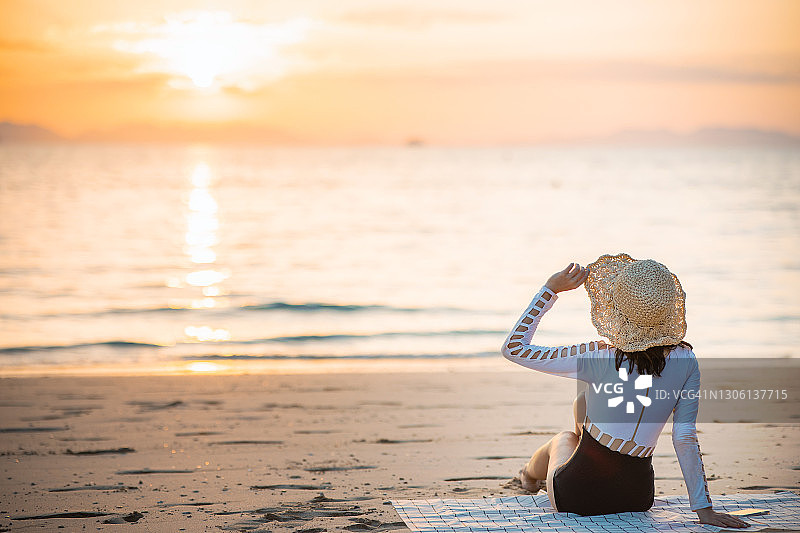年轻女子坐在泰国甲米府莱利海滩日落时分的海边图片素材