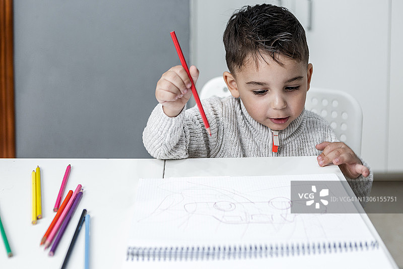 可爱的少数民族孩子在桌旁用彩色铅笔在素描本上绘画图片素材